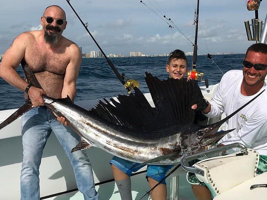 Anglers holding a sailfish across the deck aboard Spellbound off Miami