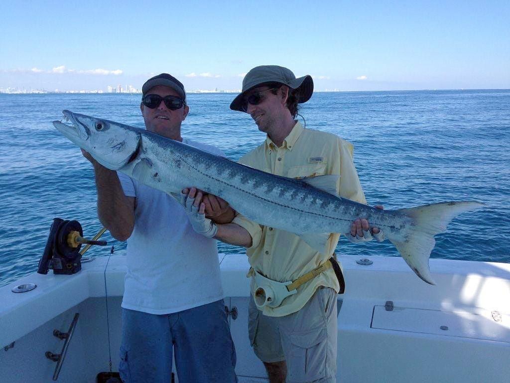 Two anglers holding a big barracuda aboard Spellbound with the Miami skyline behind
